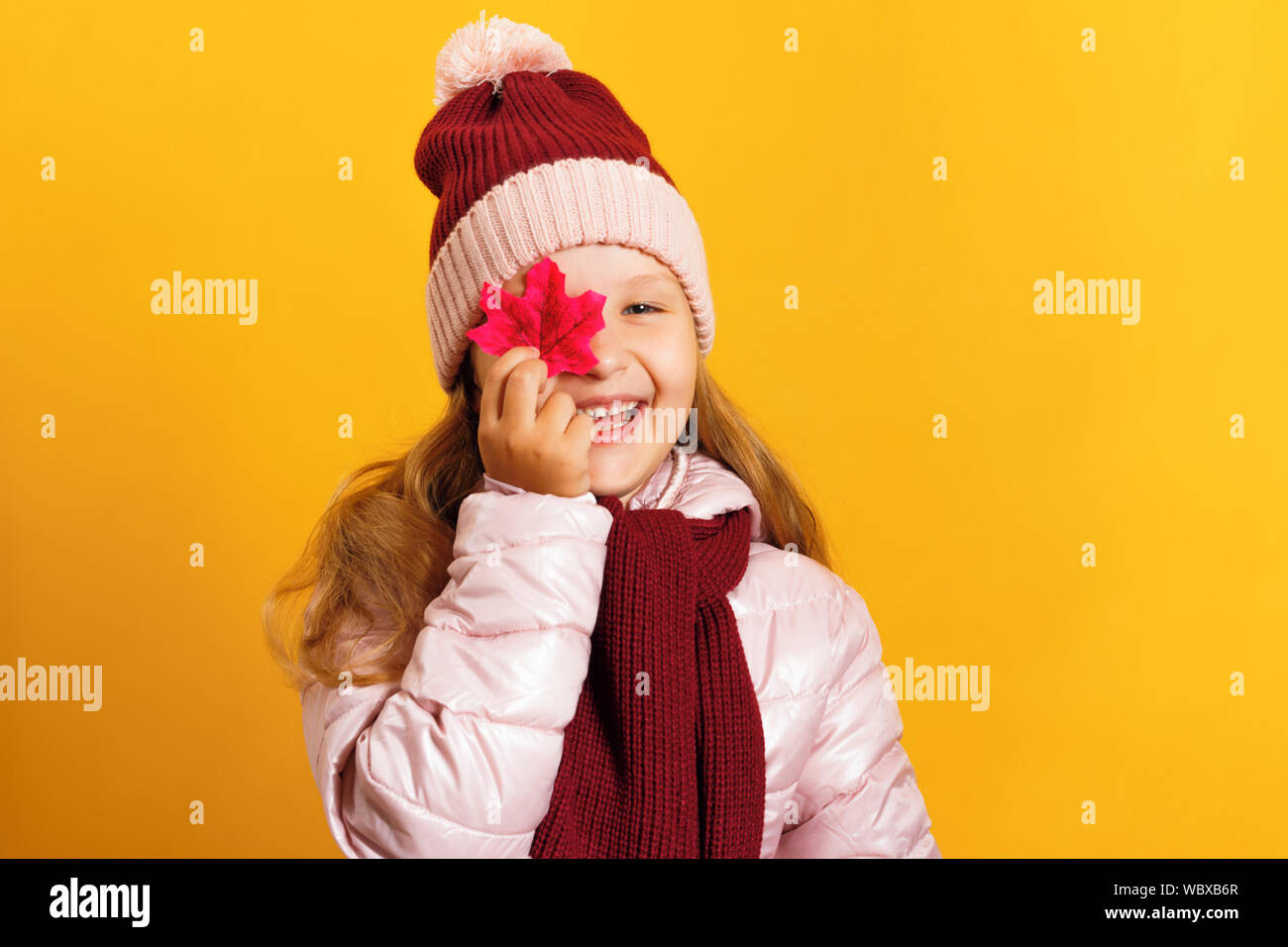 Portrait of a cute little girl dans une veste, écharpe et chapeau sur un fond jaune. L'enfant tient une feuille d'érable. Concept d'automne. Banque D'Images