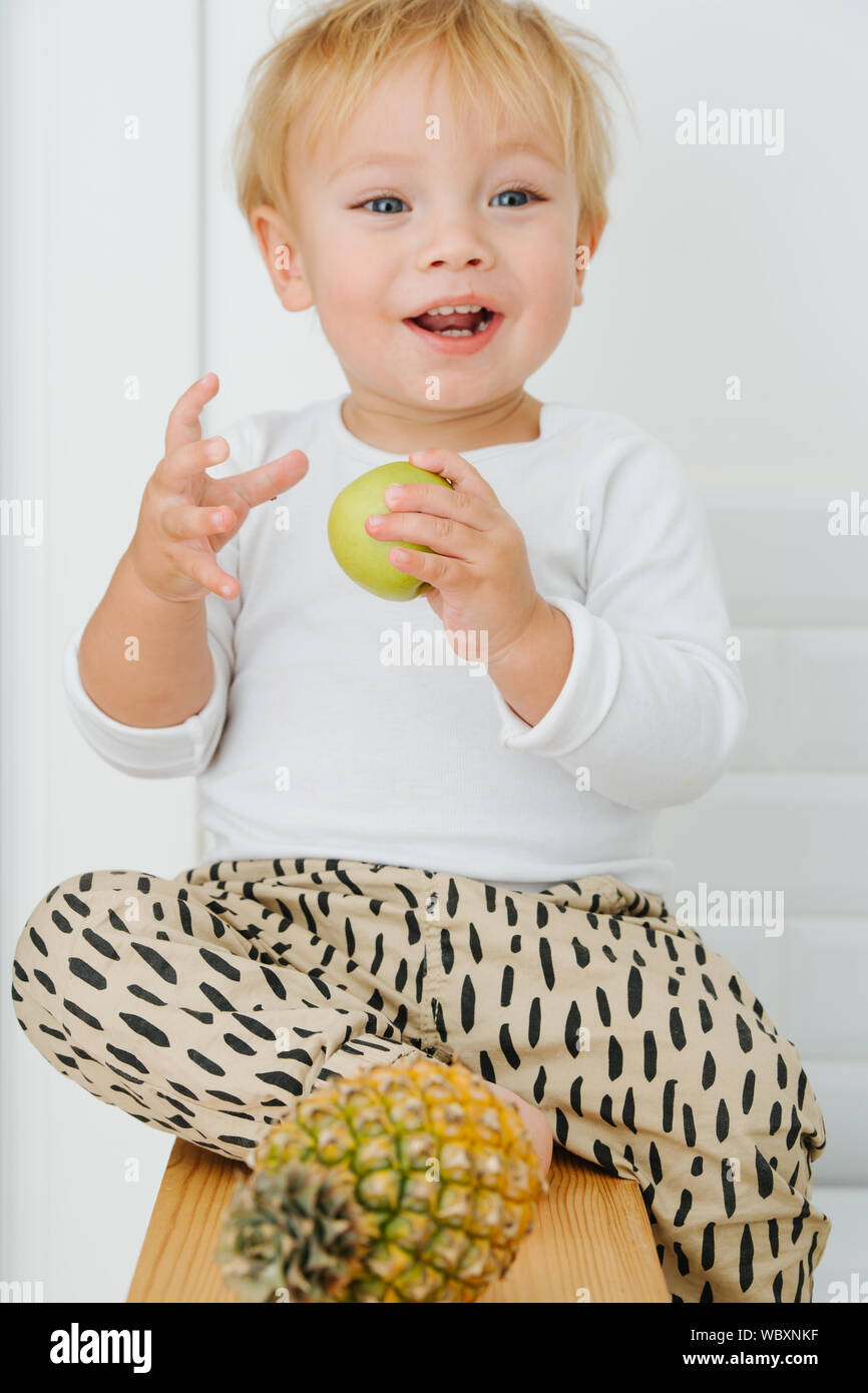 Lly blond bébé garçon est explore, joue avec des pommes de backet. Banque D'Images