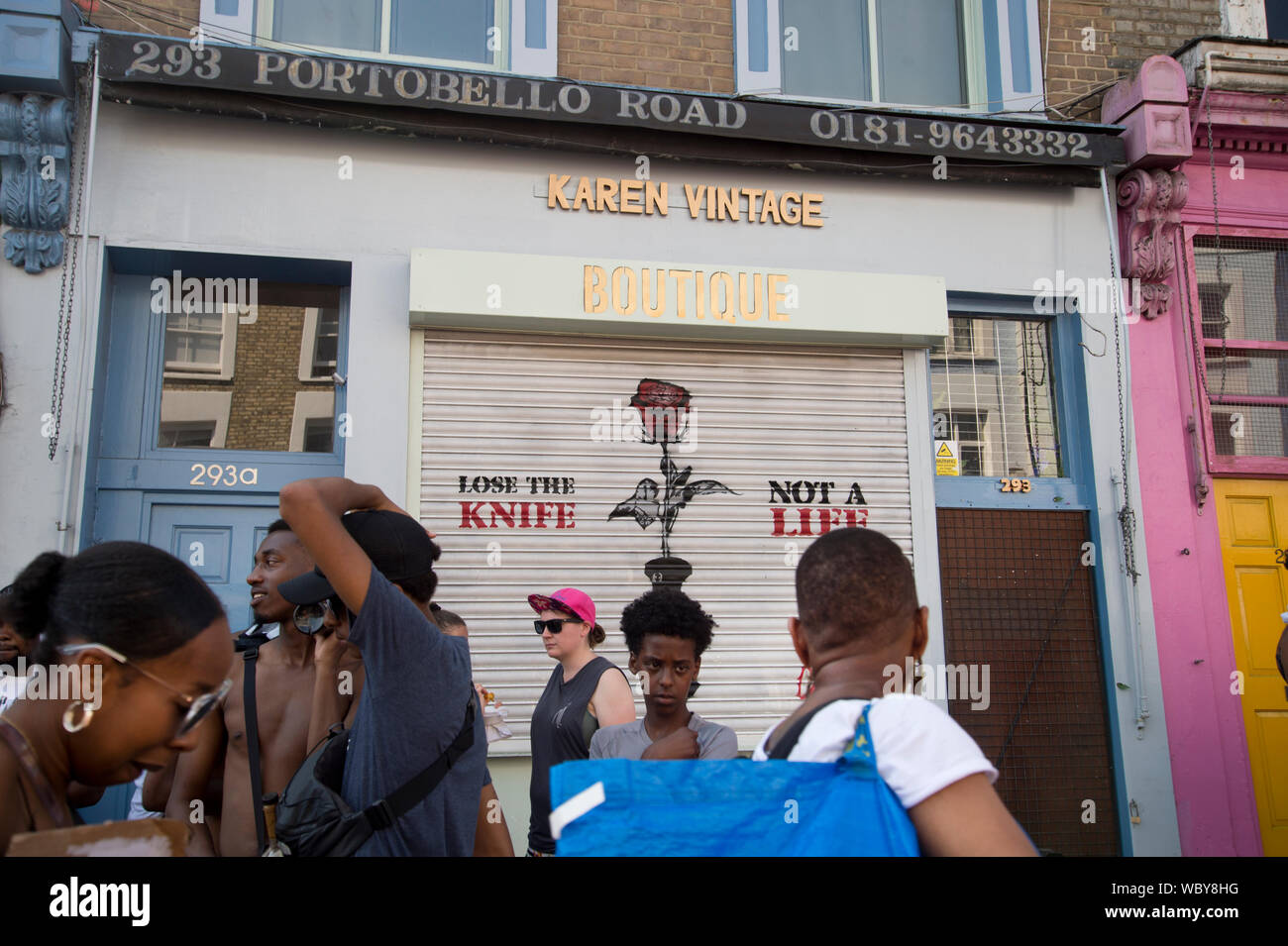 Le carnaval de Notting Hill, le 26 août 2019. Les jeunes passent devant une boutique avec le slogan "Perdre le couteau, pas une vie" peint sur son obturateur. Banque D'Images