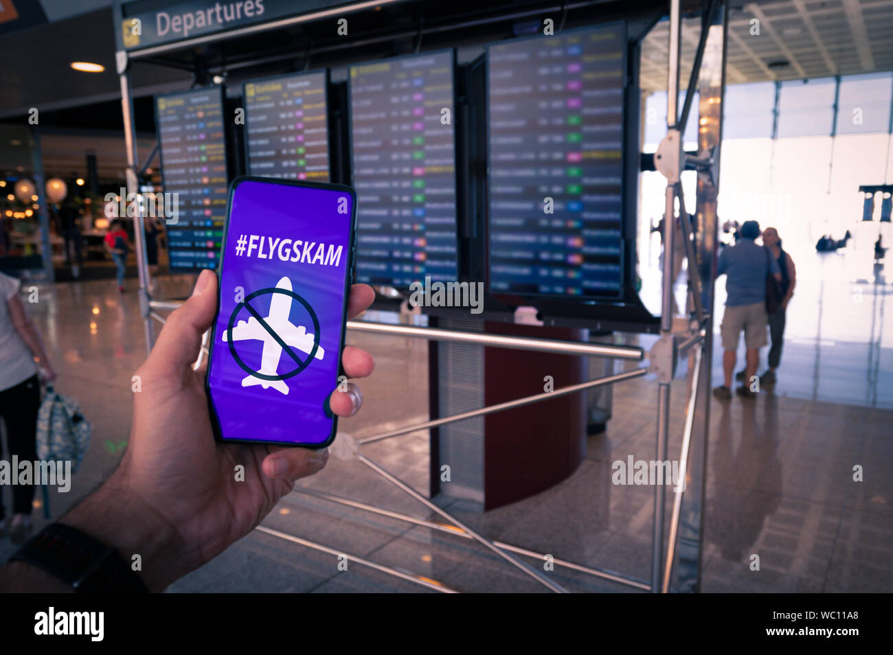 Main tenant un smartphone avec Flyskam le message à l'écran avec airport horaires en tant qu'arrière-plan. Banque D'Images