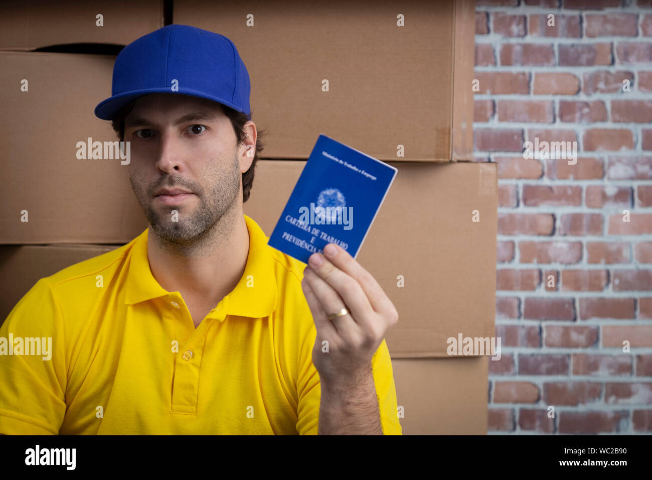 Mailman brésilien tenant son carnet de travail sécurité sociale brésilienne document, dans un dépôt avec un beaucoup de boîtes. Banque D'Images