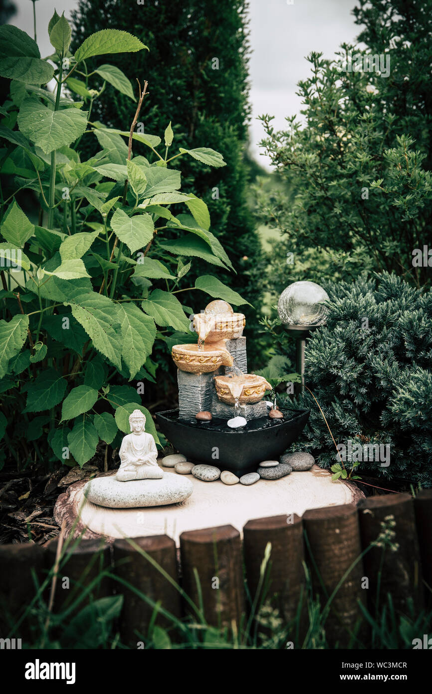 Petit jardin privé accueil fontaine avec statue de Bouddha méditant entre les arbres et arbustes. Jardin zen' concept. Banque D'Images