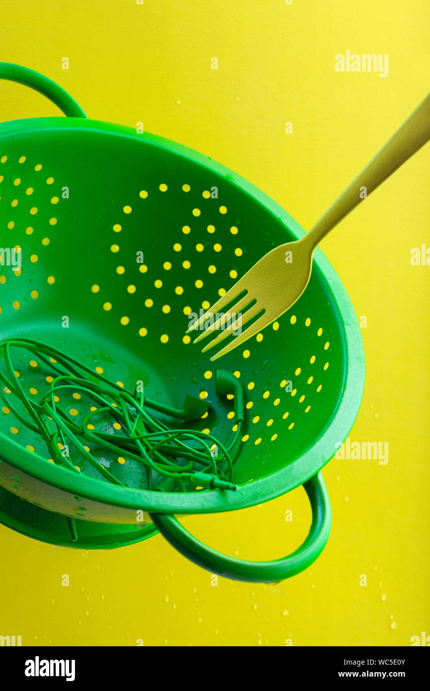 Concept créatif avec passoire verte en lévitation, branchez le casque et la fourche sur fond jaune Banque D'Images