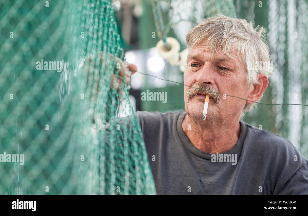 Matelot sur navire de pêche commerciale raccommodage des filets Banque D'Images