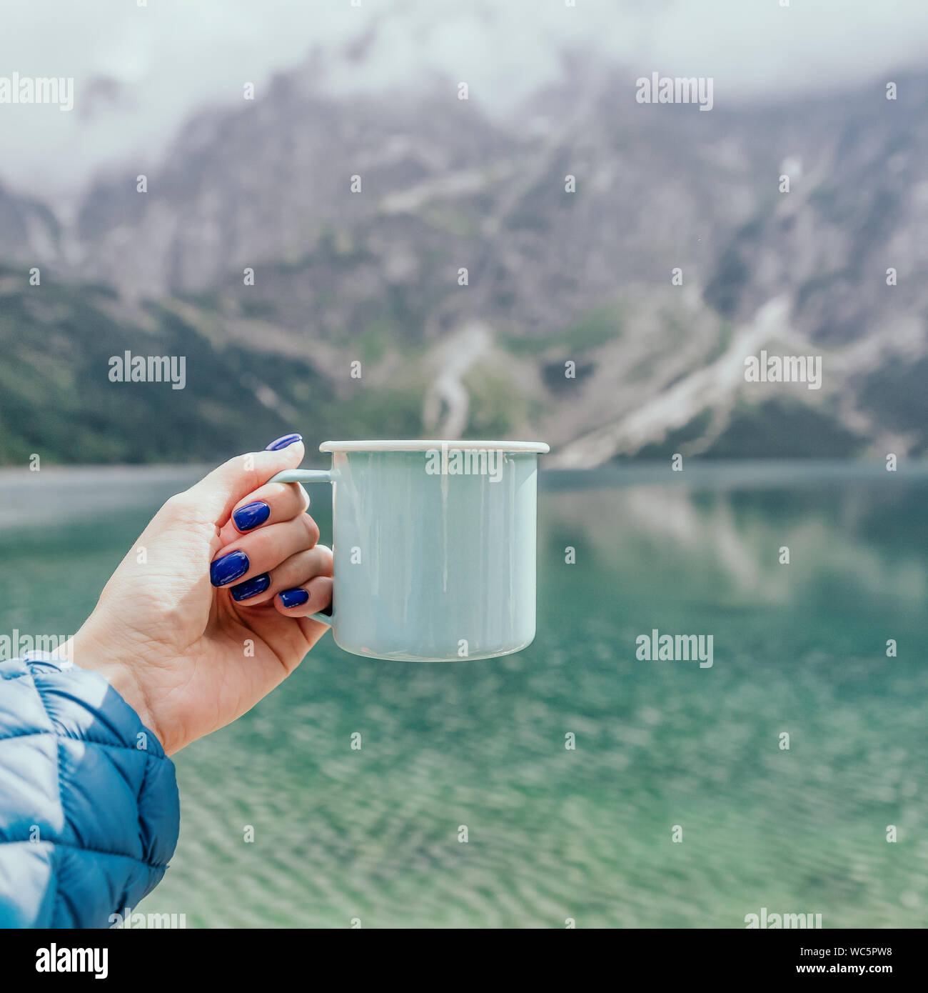 Main tenant femelle couleur menthe tasse émail. Crystal Clear Lake et les montagnes. Parc National des Tatras, en Pologne. Célèbre lac Morskie Oko ou l'oeil de la mer Banque D'Images