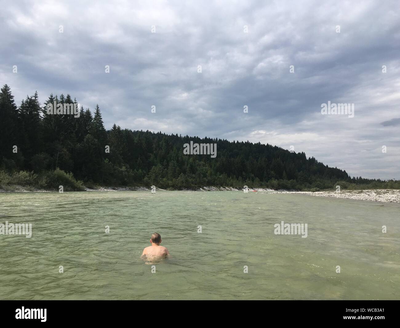 Vue arrière de l'homme nager dans le lac contre Ciel nuageux Banque D'Images