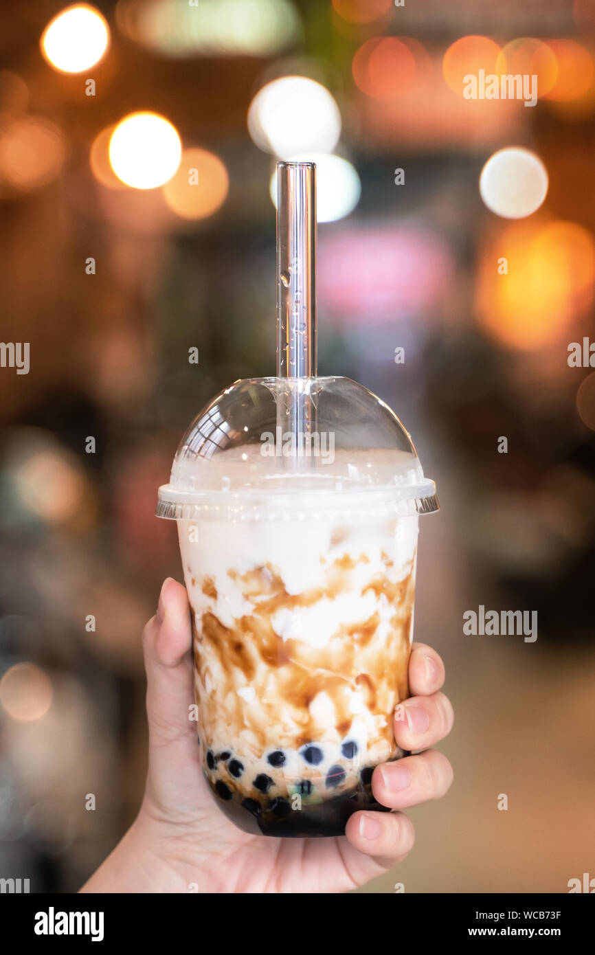 Jeune fille en denim Jacket est une consommation de sucre brun tapioca aromatisés thé lait bulle perle de verre avec paille dans marché de nuit de Taiwan, Close up, bokeh Banque D'Images