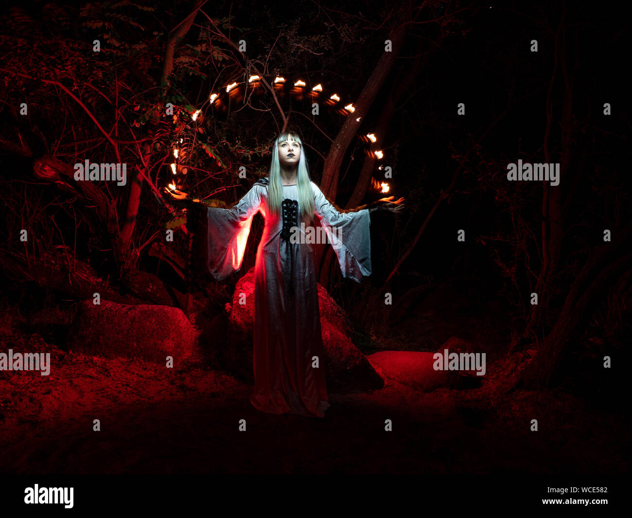 Une femme assise sur un rocher dans la forêt et vêtu d'une tunique, jette les feux rouges de ses mains. Banque D'Images