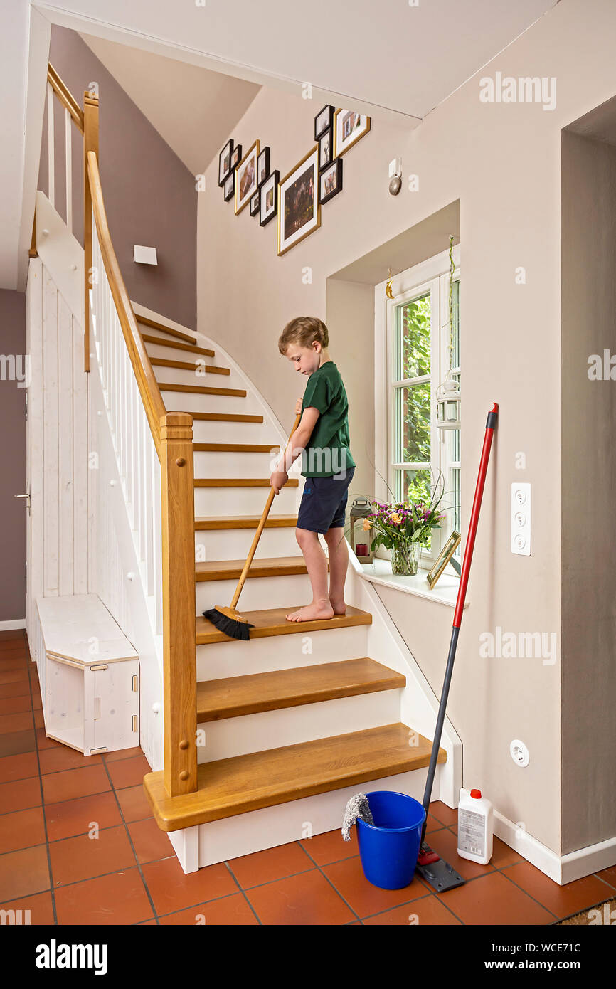 Garçon, 8 ans pour les aider à la maison dans le ménage, balayant l'escalier avec un balai. Banque D'Images