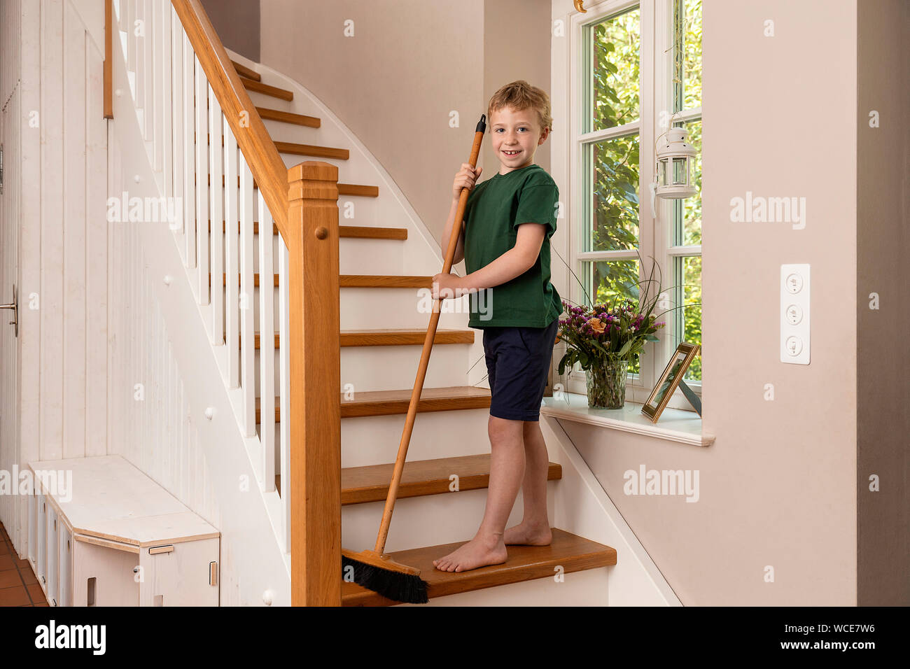 Garçon, 8 ans pour les aider à la maison dans le ménage, balayant l'escalier avec un balai. Banque D'Images