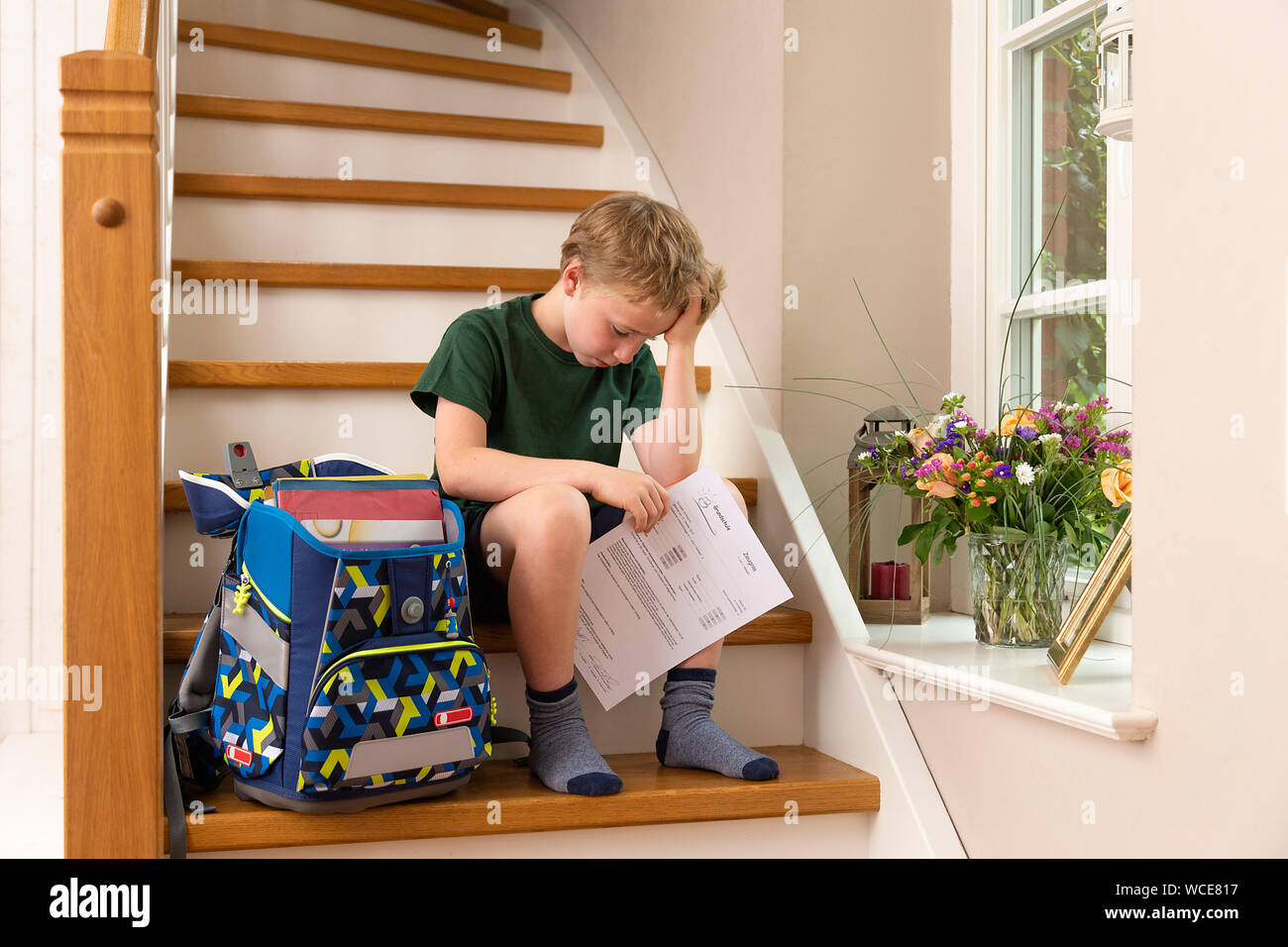 Déçu, garçon de 8 ans, à la maison avec son école primaire rapport. Banque D'Images