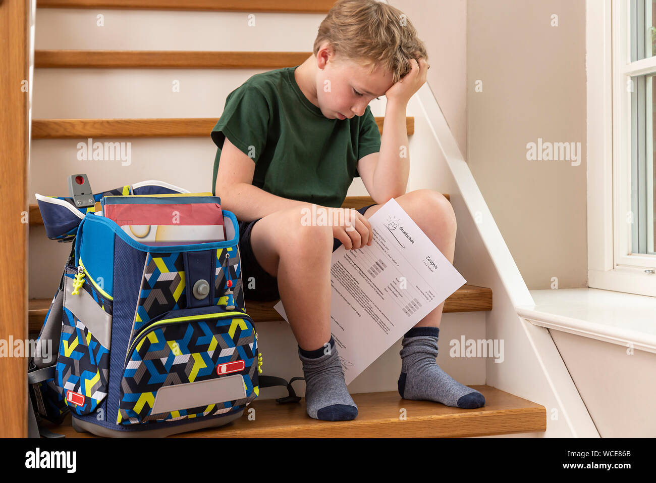 Déçu, garçon de 8 ans, à la maison avec son école primaire rapport. Banque D'Images