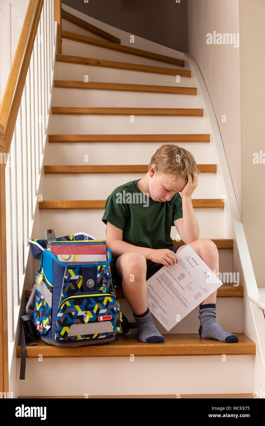 Déçu, garçon de 8 ans, à la maison avec son école primaire rapport. Banque D'Images