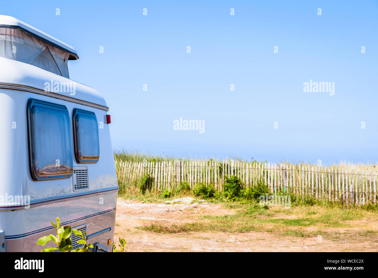 Une petite caravane avec pop-up garé sur le toit avec vue mer sur un terrain de camping délimité par une clôture en bois. Banque D'Images