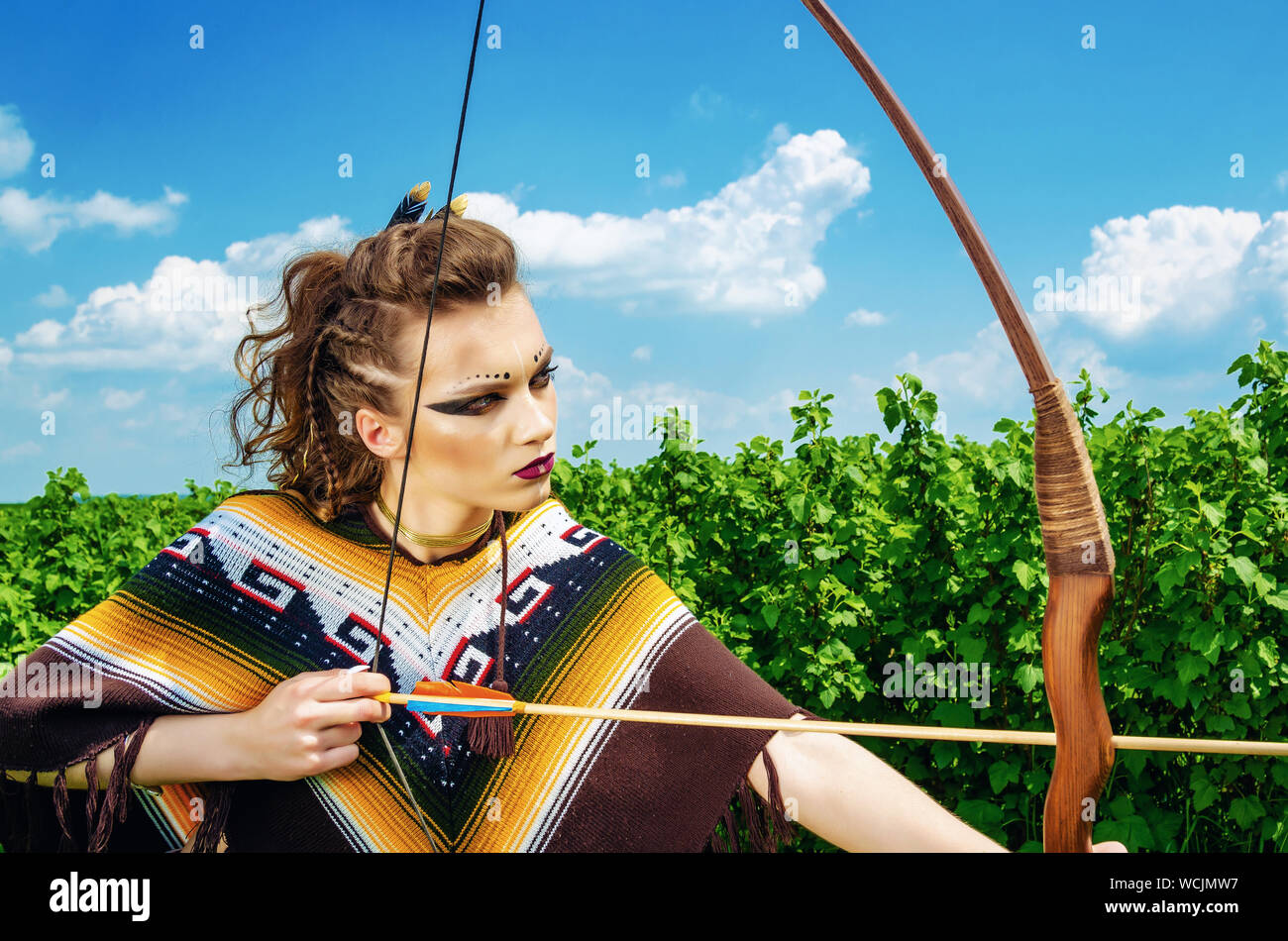 Amazon girl maquillage agressif, dans un poncho, cosplay sur le terrain,  tient un arc et des flèches. Le Paganisme, le féminisme, l'indépendance,  d'une tribu Photo Stock - Alamy