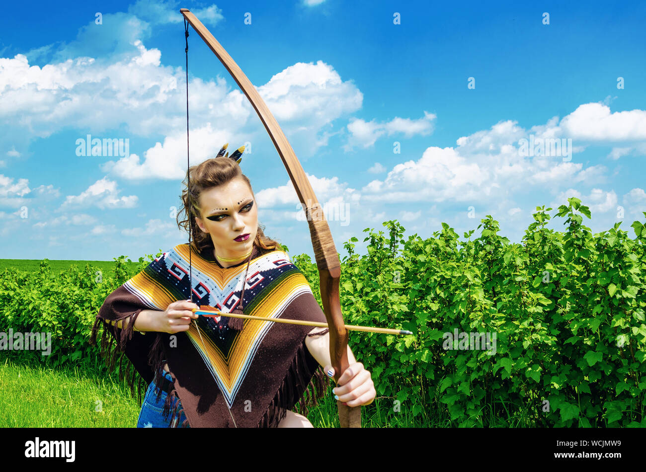 Amazon girl maquillage agressif, dans un poncho, cosplay sur le terrain, tient un arc et des flèches. Le Paganisme, le féminisme, l'indépendance, d'une tribu Banque D'Images
