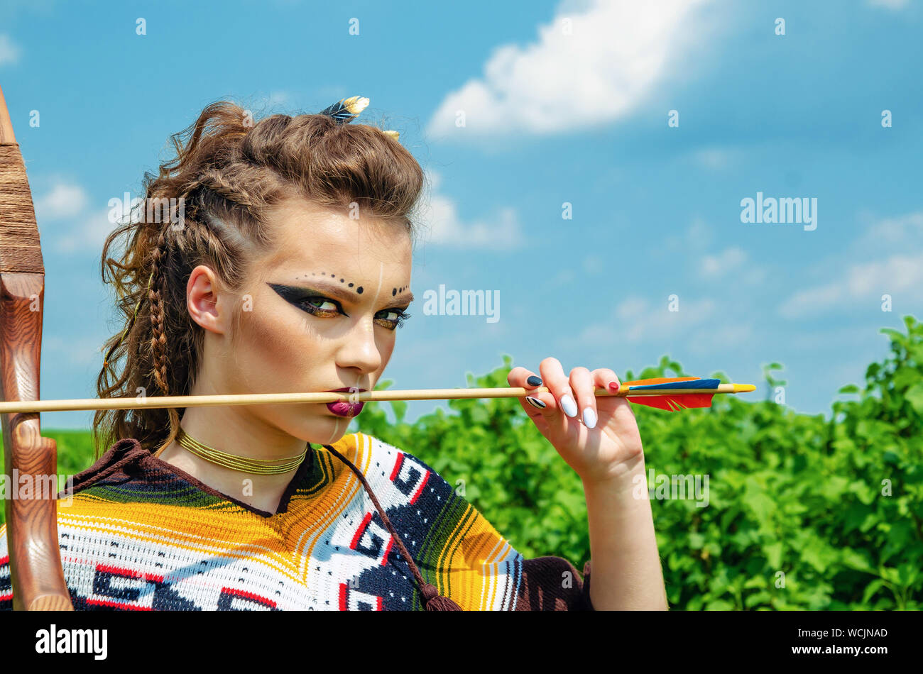 Amazon girl maquillage agressif, dans un poncho, cosplay sur le terrain, tient un arc et des flèches. Le Paganisme, le féminisme, l'indépendance, d'une tribu Banque D'Images