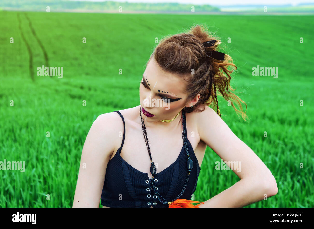Fille maquillage agressif, amazon caractère dans un champ de blé vert. Féminisme, indépendance, tribu. Banque D'Images