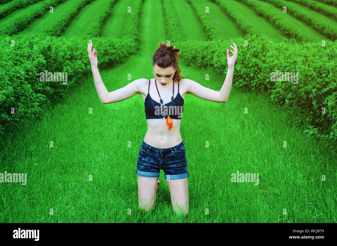 Cosplay girl maquillage agressif Viking dans un champ de blé vert. À genoux, priant pour les anciens dieux. Le Paganisme, le féminisme, l'indépendance, la tribu. Banque D'Images