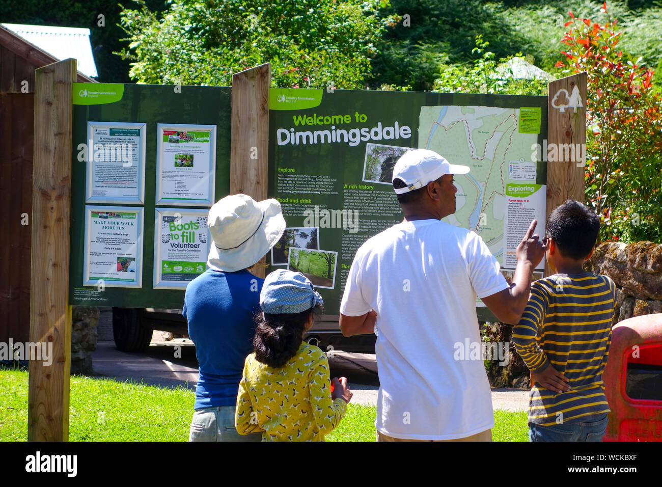 Une famille noire regardant le tableau d'affichage à l'entrée de Dimmingsdale ou Dimmings Dale, près d'Oakamoor, Staffordshire, Angleterre, Royaume-Uni Banque D'Images