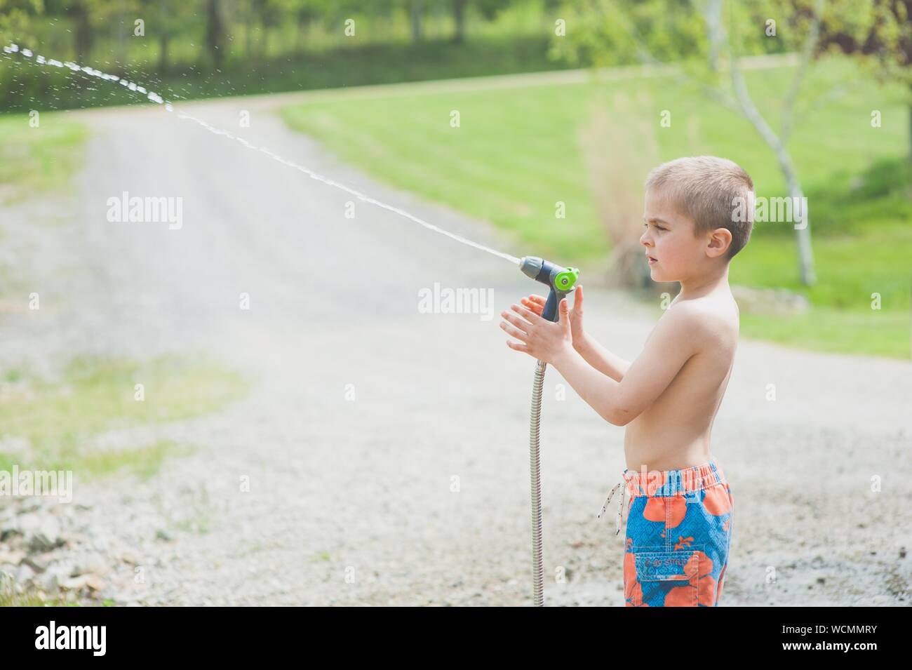Gros plan d'un jeune garçon dans un maillot de bain avec un arroseur extérieur par beau temps Banque D'Images