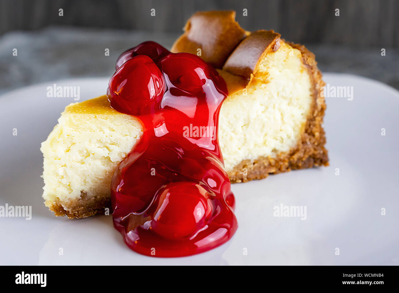 Une tranche de gâteau au fromage style New York avec la sauce aux cerises. Plan rapproché sur une plaque blanche. Arrière-plan flou neutre. Banque D'Images