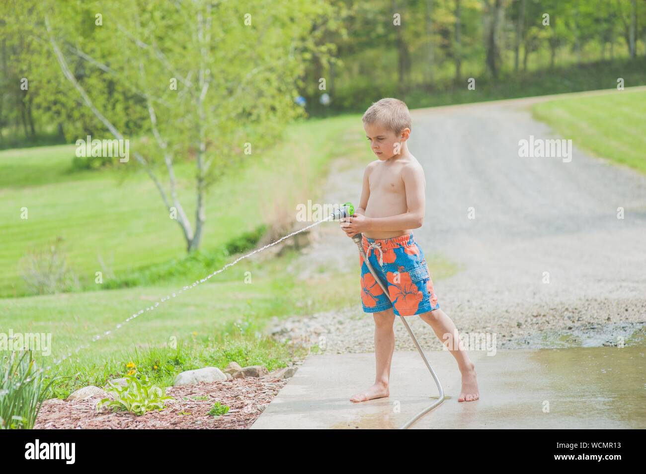 Gros plan d'un jeune garçon dans un maillot de bain avec un arroseur extérieur par beau temps Banque D'Images