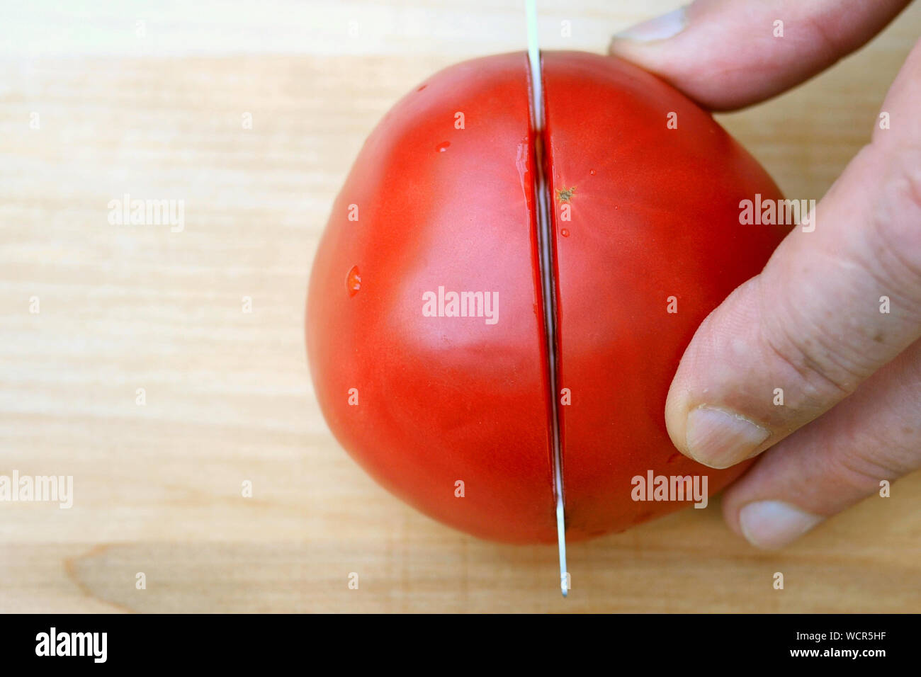 La main de couper la tomate rose rouge, avec des couteaux de cuisine, sur la surface en bois pour la cuisine. Close-up. Banque D'Images