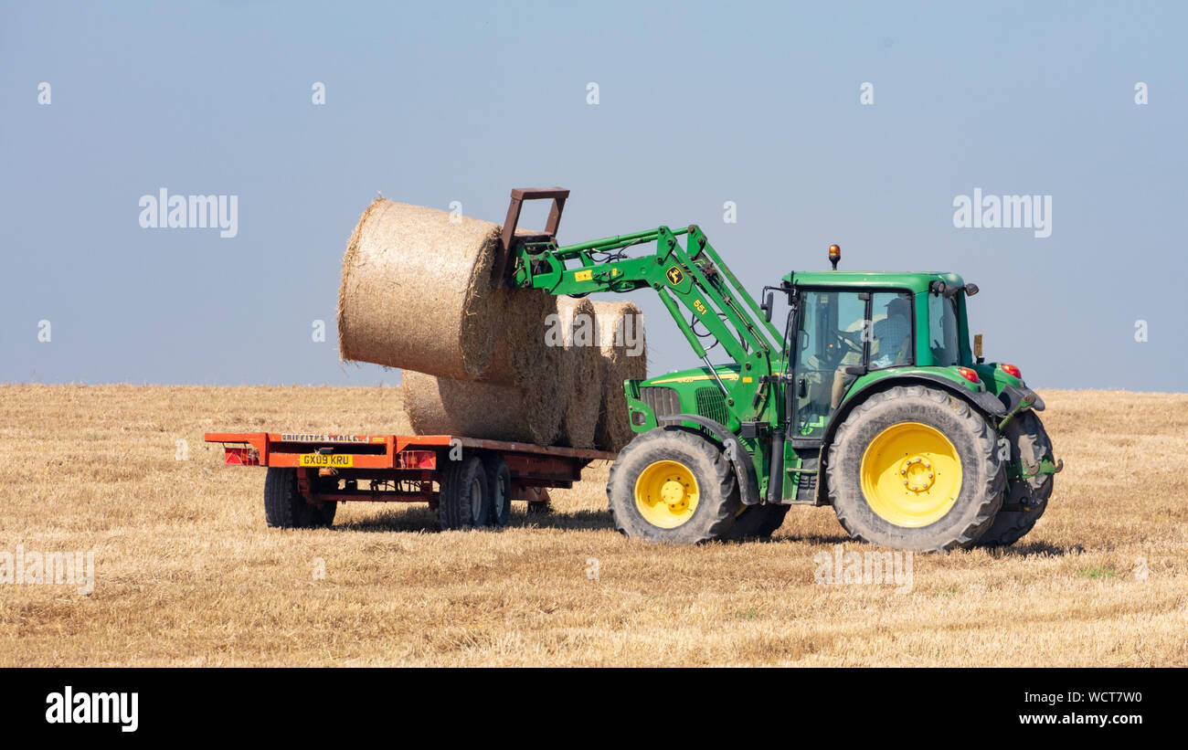 Près de Devils Dyke, Brighton, Royaume-Uni ; 26 août 2019 ; Farmer dans un tracteur en mouvement des balles de foin sur une remorque à fond plat pour le transport sur une journée brumeuse lumineux Banque D'Images