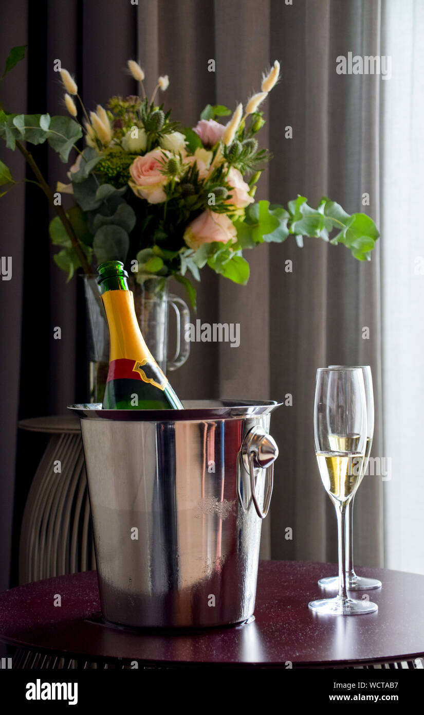 Date romantique avec open champagne et verres de champagne sur la table avec bouquet de fleurs fraîches dans un vase à l'arrière-plan Banque D'Images