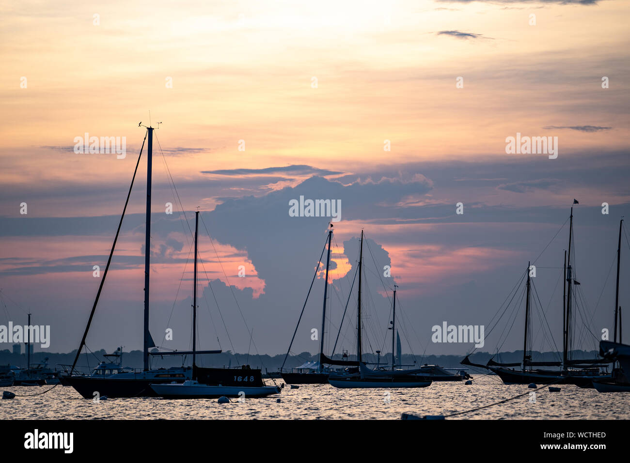 Voiliers en silhouette sur leurs mouillages au coucher du soleil, regard vers l'ouest à travers le Newport Harbor en direction de Jamestown, Newport, Rhode Island, États-Unis. Banque D'Images