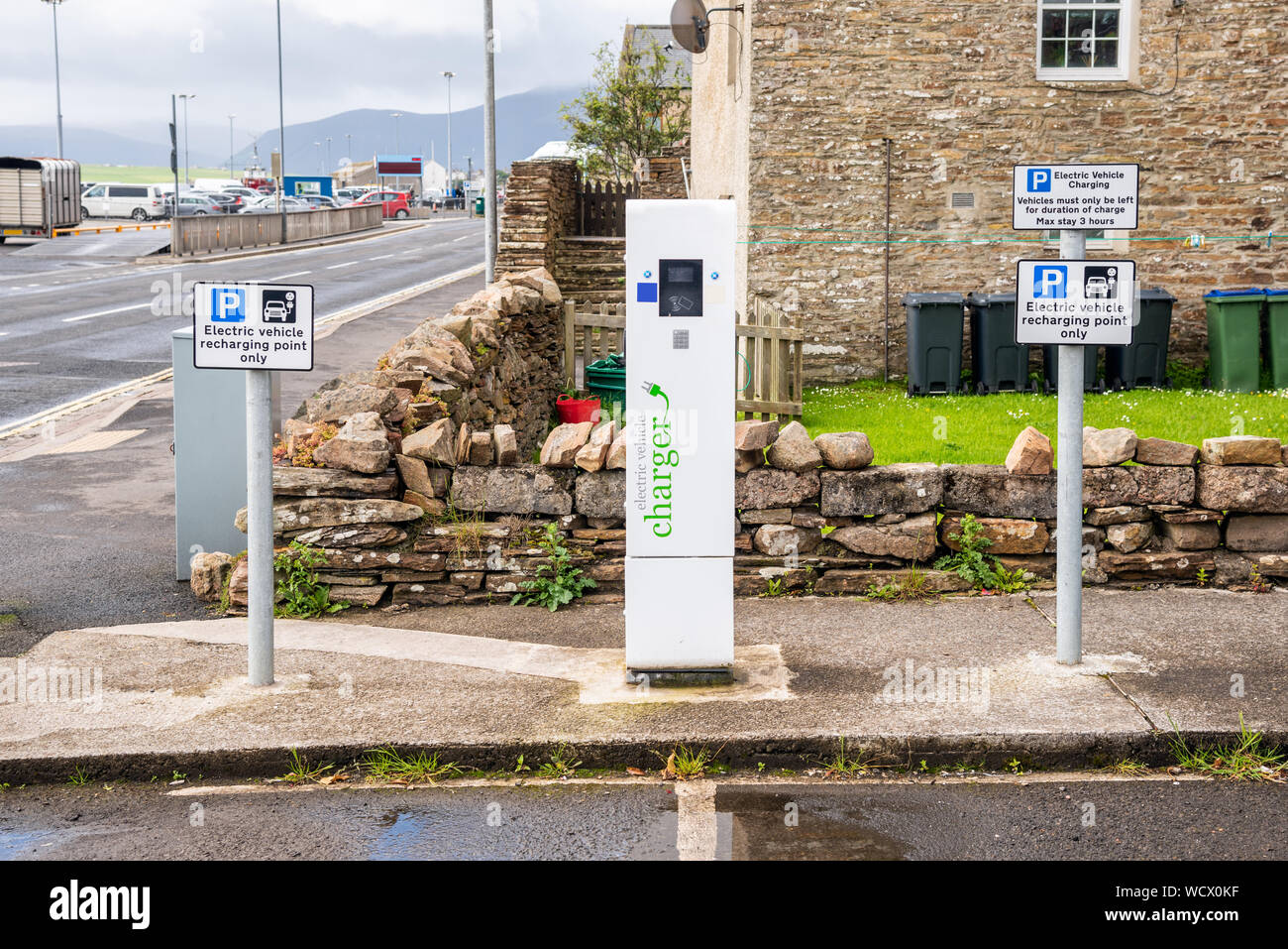 Voiture électrique point de recharge avec un chargeur et panneaux de stationnement le long d'une rue sur une journée d'été nuageux Banque D'Images