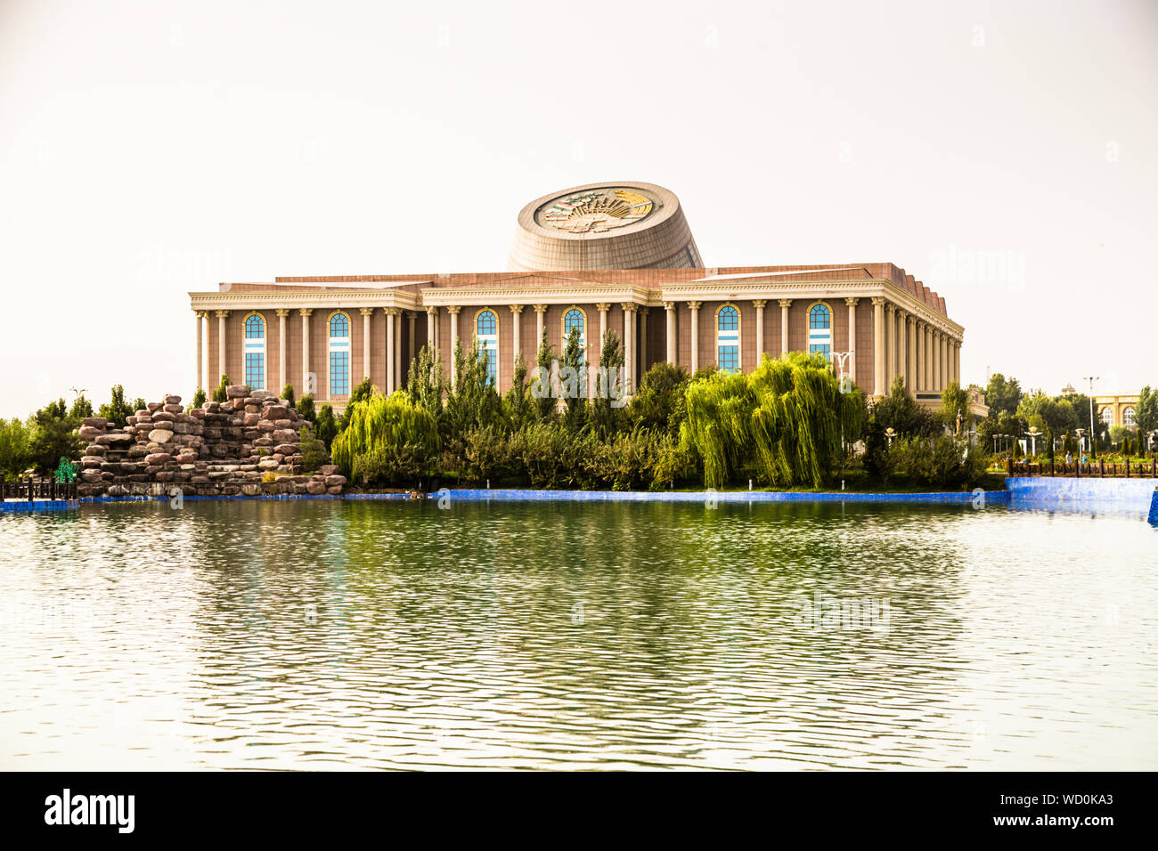 Le Musée national du Tadjikistan se reflète dans un lac artificiel à Douchanbé, au Tadjikistan, sa lucarne ovale en forme de dôme se mirant dans l'eau, une cascade de rochers empilés éclaboussant au rivage. Banque D'Images