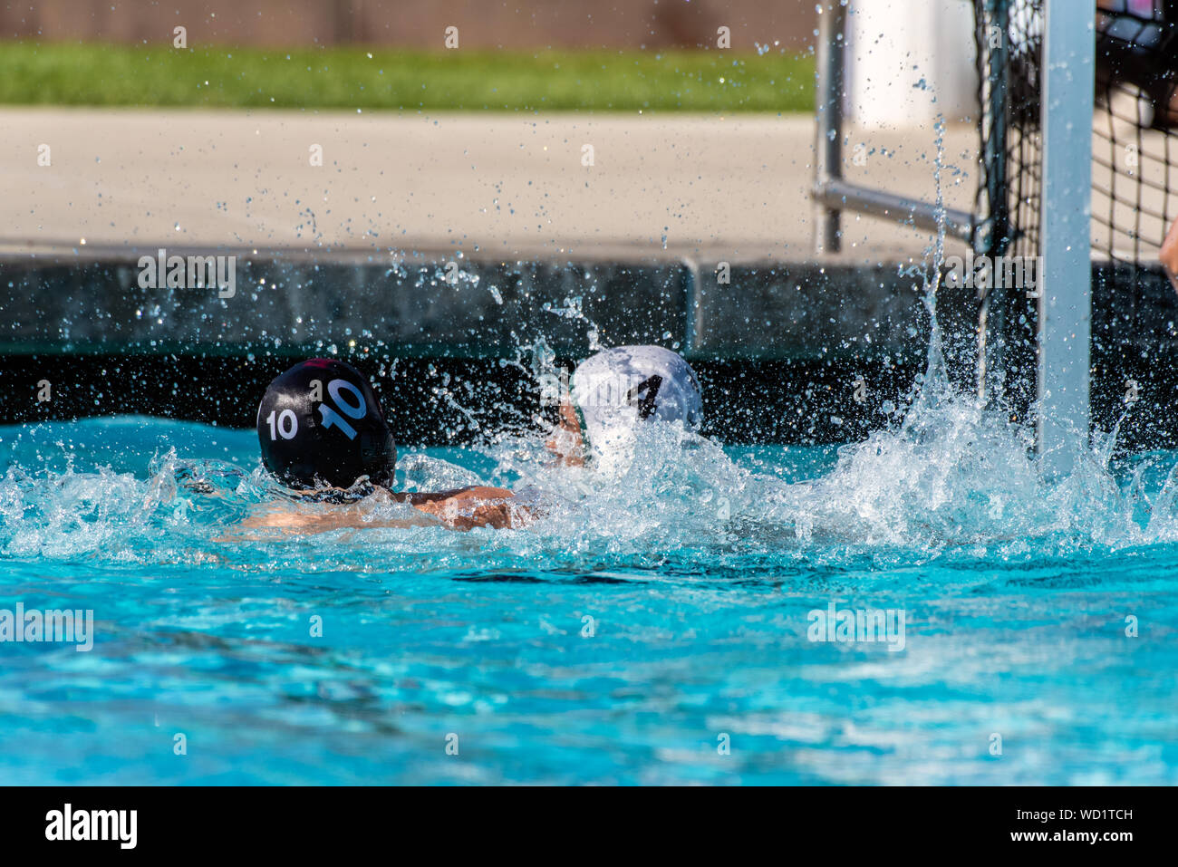 10 Numberr dans black water-polo batailles uniforme avec grand effort et éclaboussures contre numéro 4 en uniforme blanc au cours de match. Banque D'Images