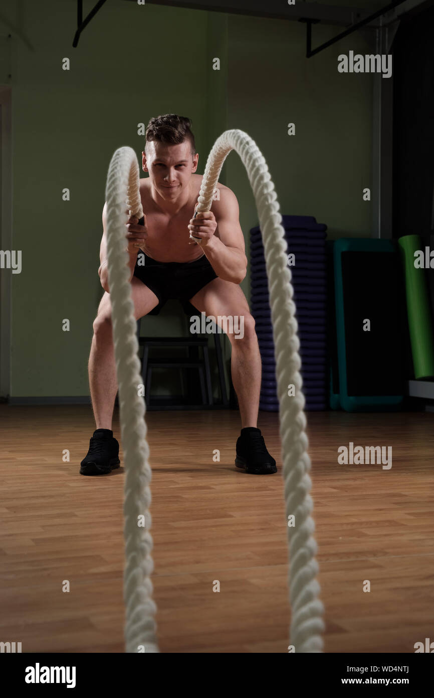 Jeune homme athlétique avec corde bataille faire de l'exercice dans la salle de sport fitness formation fonctionnelle. Banque D'Images