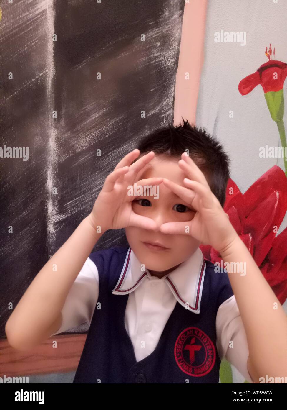 Portrait de garçon avec des yeux les mains contre le port de l'uniforme  scolaire Photo Stock - Alamy
