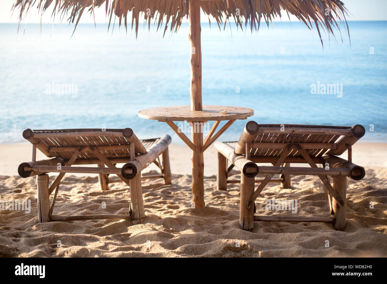 Deux chaises longues et table en bambou vide sous parapluie de paille sur la plage de sable blanc, mer bleu solitaire fond dans le soleil du matin la lumière, personne ne Banque D'Images