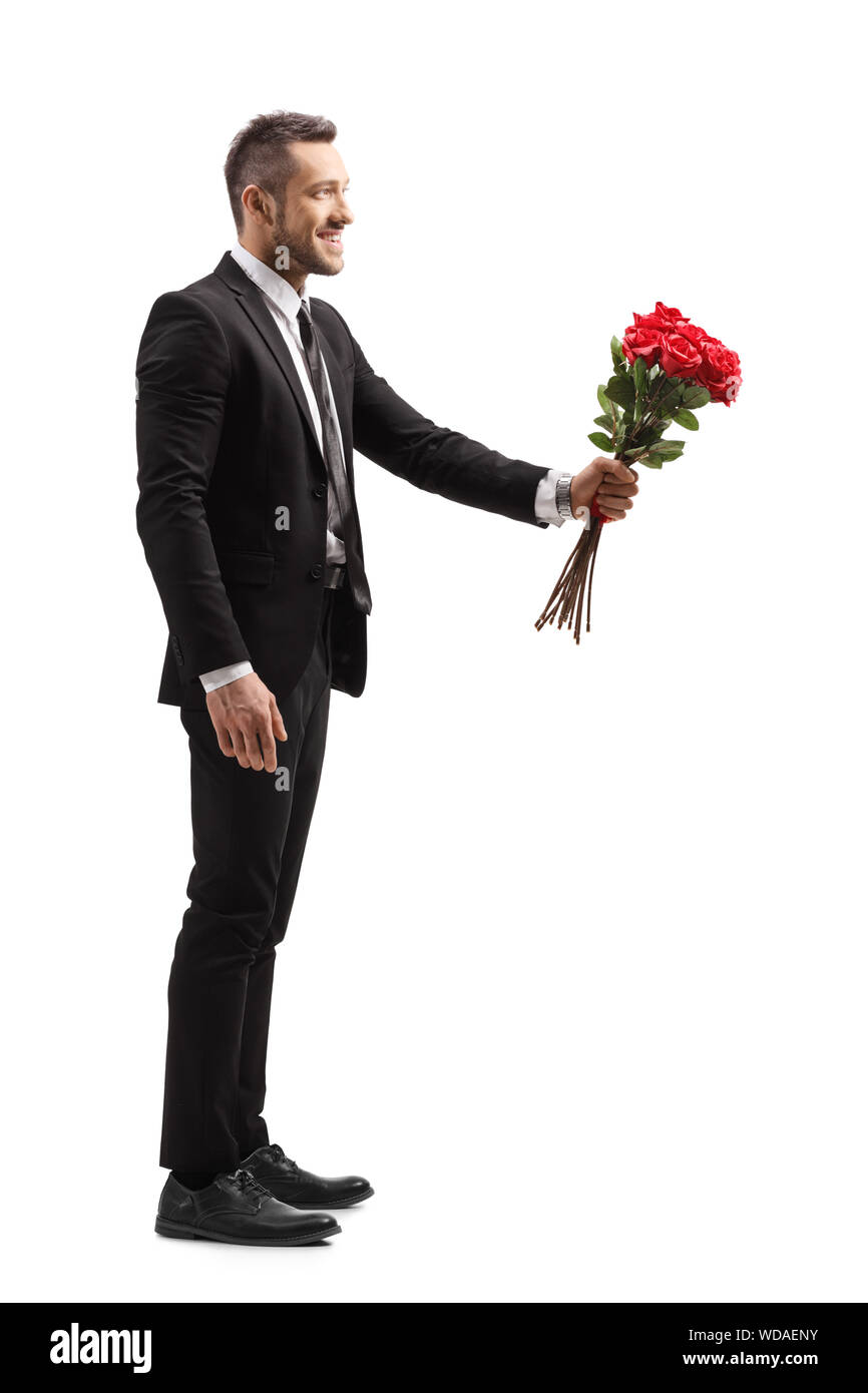 Profil de pleine longueur de balle un jeune homme élégant de sourire et de donner un bouquet de roses rouges isolé sur fond blanc Banque D'Images