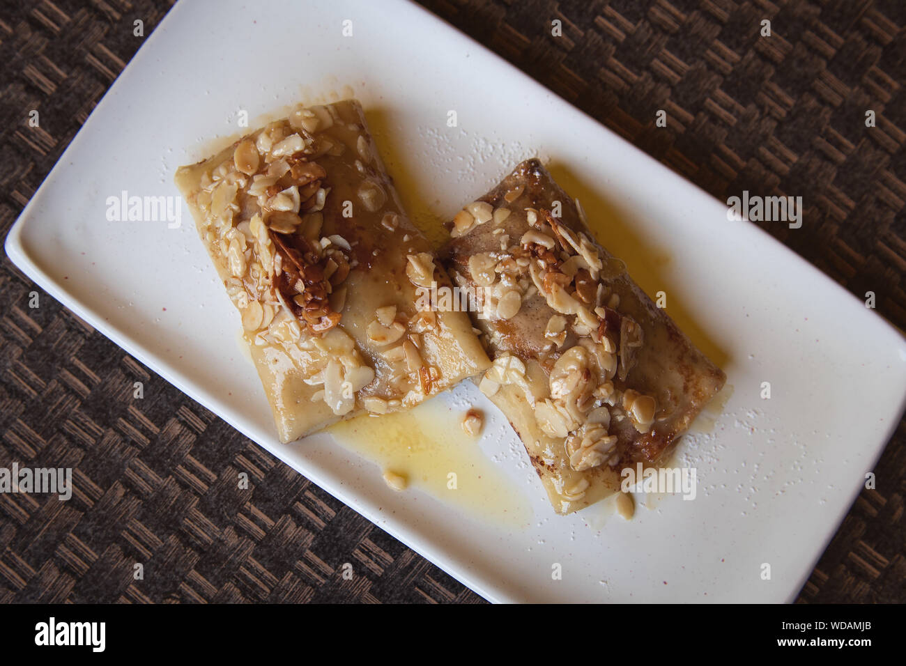 Crêpes russes avec du fromage cottage et de remplissage des amandes tranchées et de miel sur le dessus. Délicieux dessert sur la plaque blanche. Banque D'Images