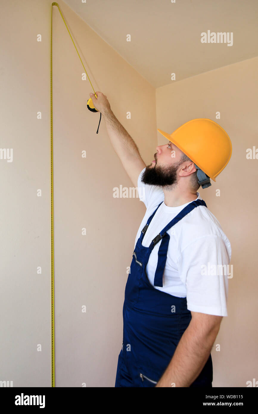 Travailleur de la construction et l'homme travaille sur la rénovation d'appartement. Builder est la mesure de la paroi, à l'aide de ruban de mesure au chantier de construction. Banque D'Images