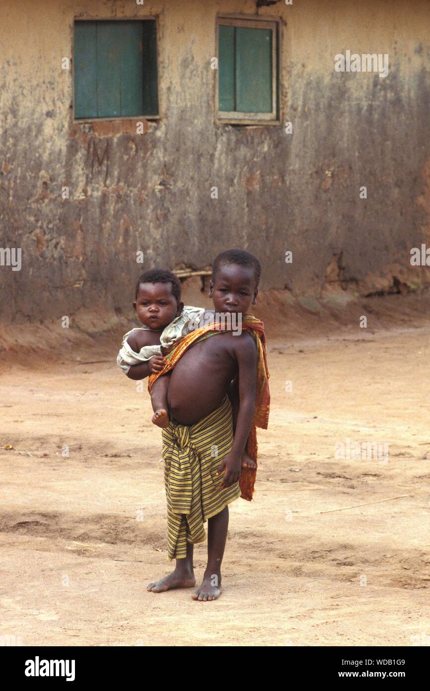 KINSHASA, CONGO, RÉPUBLIQUE DÉMOCRATIQUE DU - Aug 08, 1980 : African Child holding baby avec l'environnement urbain pauvre Banque D'Images