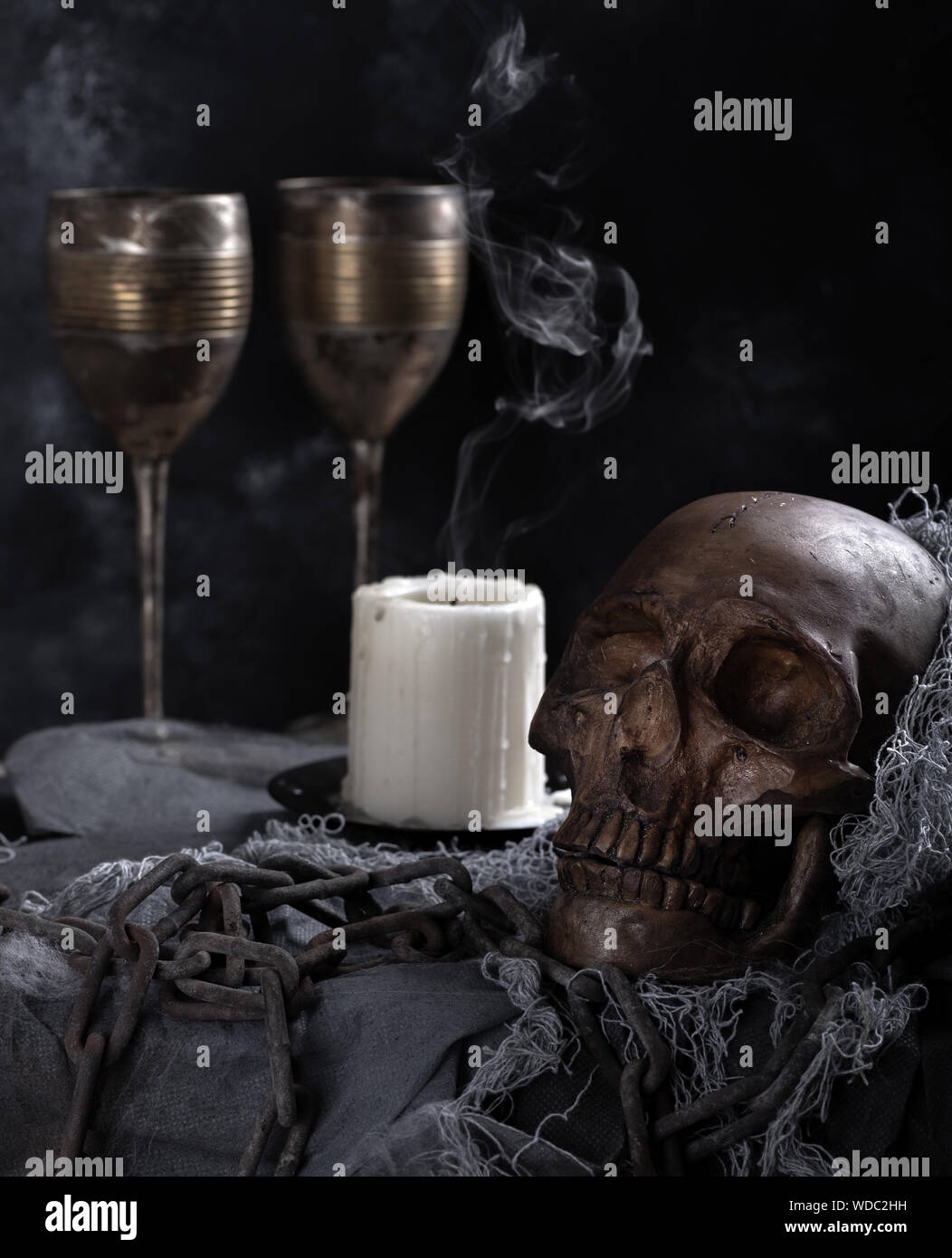 Crâne humain effrayant avec bougie couvant et gobelets vintage dans un fond sombre. Banque D'Images