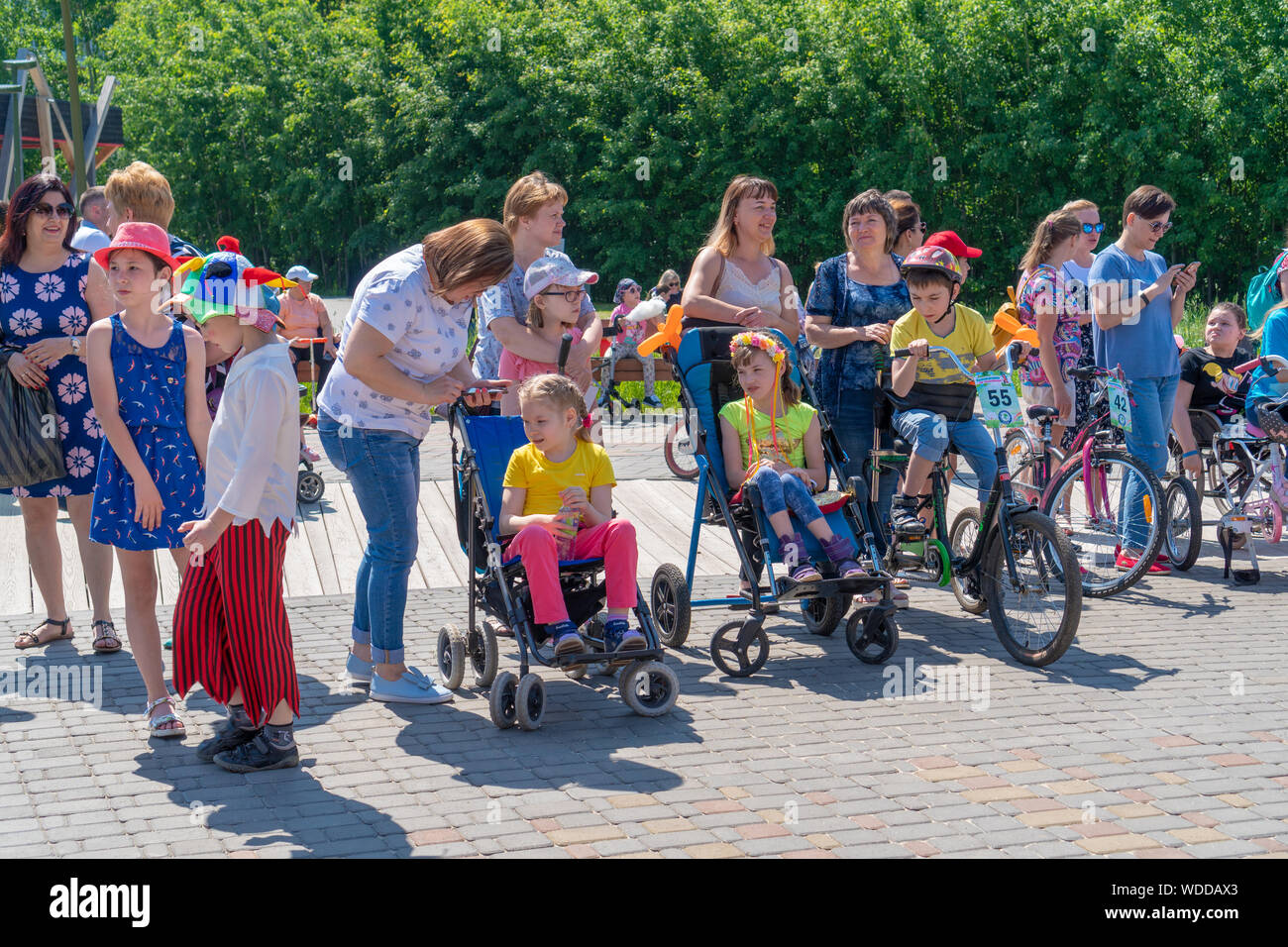 La Russie, Kazan - 31 mai 2019 : Mobilité garçon avec des lunettes sur un vélo à quatre roues sur une journée ensoleillée. Les filles en fauteuil roulant regarder une balade à vélo. Ch Banque D'Images