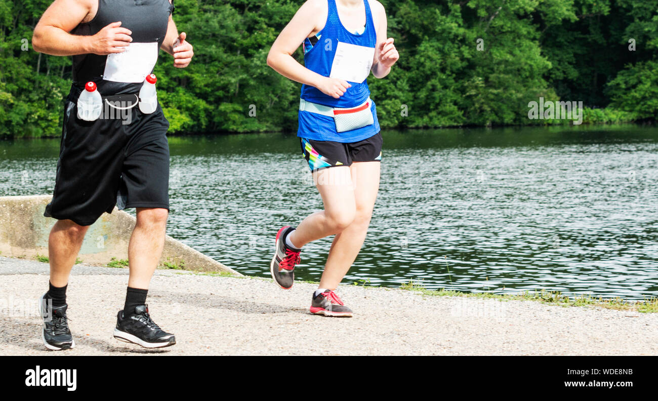 Un homme et une femme sont en cours d'exécution à côté de l'autre dans les bois en passant un lac sur un chemin de terre. Banque D'Images