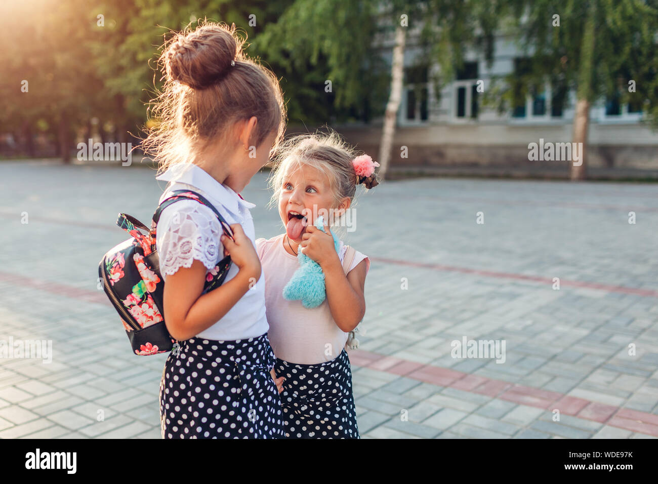 Heureux soeurs filles portant des sacs à dos et d'avoir du plaisir. Les élèves après les cours pour les enfants à pied à l'extérieur de l'école primaire. L'éducation. Retour à l'école Banque D'Images