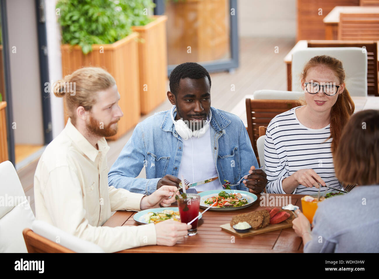 Groupe de jeunes multiethniques assis à la table et de parler les uns aux autres pendant que le déjeuner au restaurant Banque D'Images