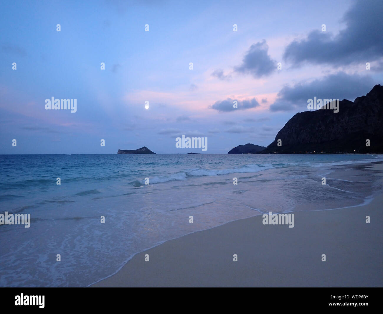 Gentle wave tour sur Waimanalo Beach à Rabbit island, vers l'île de roche, et la pleine lune accroché au-dessus de lui à la tombée sur une Oahu, Hawaii. Août 2015. Banque D'Images