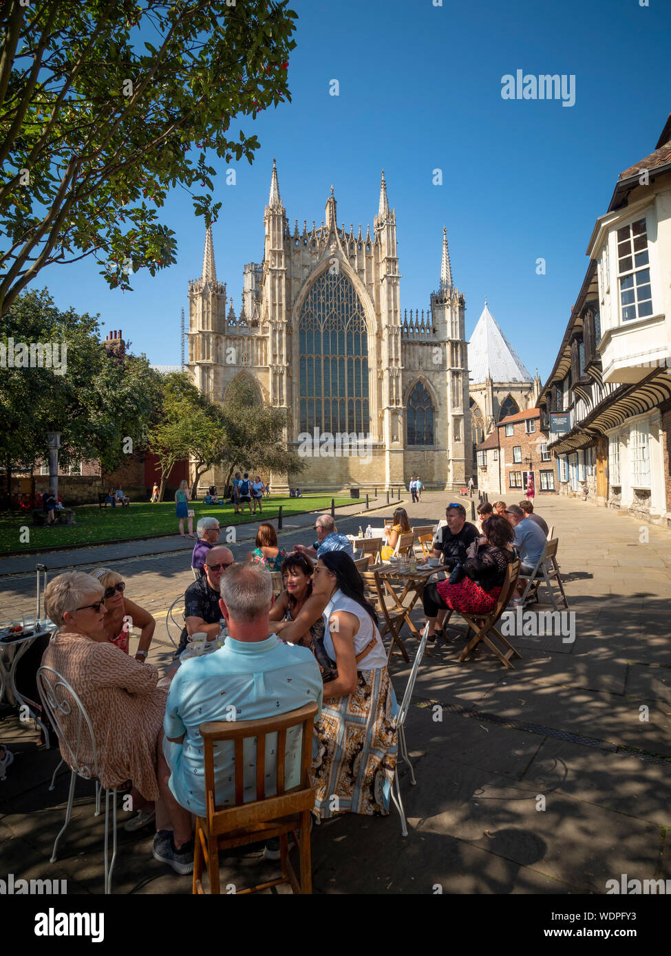 Les gens assis dehors au café avec York Minster et St Williams College en arrière-plan, la rue College, York, Royaume-Uni. Banque D'Images