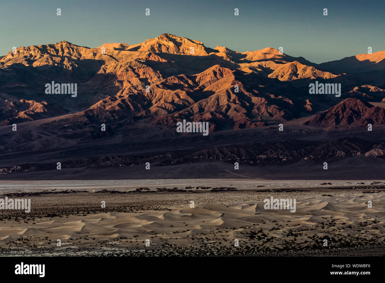 Le coucher du soleil illuminant dé à pic dans la Death Valley National Park avec Mesquite Sand Dunes en premier plan Banque D'Images