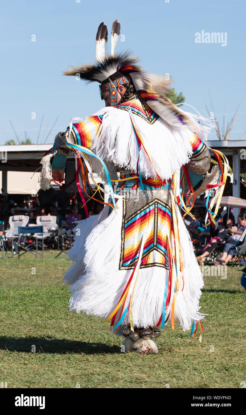 Jeune homme originaire de danser dans un pow-wow dans une white fringed garment avec des rubans et des dessins géométriques et de plumes et de la fourrure. Banque D'Images